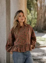 Camisa de lino con estampado floral en tonos tierra y rojizos, de corte amplio con volado en la cintura y mangas largas abullonadas con puños elásticos.