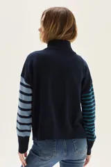 Sweater de cuello tortuga, tejido a rayas horizontales azul marino y blanco. Presenta un bordado de flor roja en el pecho y mangas largas con diseño de rayas en tonos de azul más claro.