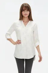 Blusa de viscosa color blanco con estampado sutil, cuello en V y mangas 3/4 con presilla para arremangar. Presenta un bolsillo aplicado en el pecho y un diseño de corte largo y redondeado en el dobladillo.