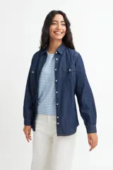 Camisa de denim azul con dos bolsillos frontales con botón, corte recto y mangas largas con puños abotonados.