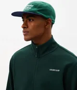 Buzo deportivo Get Over de color verde oscuro, confeccionado en tejido de algodón y poliéster. Presenta cuello alto, cierre frontal completo con cremallera, mangas largas con puños ajustados y bolsillos laterales. Incluye un pequeño lettering bordado en el pecho.