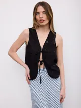 Chaleco negro sin mangas, confeccionado en tejido broderie con detalles perforados, escote en V y cierre frontal con tiras para atar.