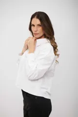 Camisa blanca de corte recto y largo cropped, con cuello clásico, cierre frontal de botones y mangas largas con puños abotonados. Presenta un sutil estampado de pequeños puntos distribuidos por toda la prenda.