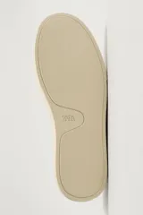 Mocasín casual de cuero negro con textura granulada, diseño sin cordones y suela de goma a contraste en color beige.