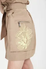 Minifalda color tostado de tejido tecnológico con cierre frontal con cremallera metálica, bolsillos laterales con fuelle y lazo en la cintura.