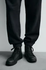 Zapatilla tipo botín de estilo minimalista fabricada en piel lisa de color negro. Presenta un diseño de caña media con cierre de cordones al tono y suela plana de goma a juego.