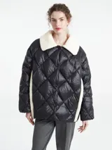 Chaqueta negra capitoneada con diseño de rombos, cuello de corderito blanco y paneles laterales de corderito a tono. Presenta cierre frontal con botones a presión.
