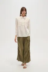 Camisa de manga larga color celeste, con cuello camisero y cierre frontal de botones. Presenta un diseño distintivo con paneles de encaje tipo crochet en la parte superior delantera.