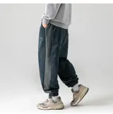 Pantalón tipo babucha de tela marrón tipo gamuza, con cintura elástica y cordón ajustable, puños ajustados en los tobillos y una franja lateral de color beige.