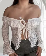 Top de encaje blanco con mangas largas acampanadas, hombros descubiertos, volados y lazo ajustable en el frente.