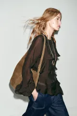 Bolso tipo saca de diseño asimétrico confeccionado en piel de ante. Cuenta con un asa bandolera ajustable, cierre mediante imán y un bolsillo interior con cremallera.