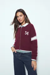 Campera de punto tipo cardigan en color bordó, con cierre frontal, cuello redondo y diseño estilo universitario. Presenta el número 54 bordado en blanco en el pecho y franjas blancas en las mangas.