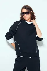 Hoodie negro con capucha y ribetes blancos decorativos en la parte frontal y mangas.