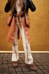 Pantalón de cuero color beige con costuras decorativas en forma de cruz a lo largo de las piernas.