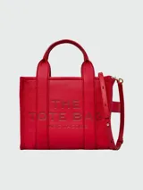 Cartera tipo tote de cuero rojo de la marca Marc Jacobs, modelo The Leather Small Tote Bag. Presenta doble asa superior, correa ajustable y extraíble para el hombro, y el texto grabado en relieve "THE TOTE BAG MARC JACOBS" en el frente.