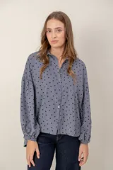 Camisa de corte oversize y diseño holgado, color celeste con estampado de pequeños corazones negros. Presenta cuello clásico, cierre frontal con botones y mangas largas abullonadas con puños ajustados.