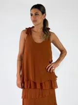 Top de viscosa color marrón tostado, sin mangas, con escote redondo y detalle de lazos para anudar en los hombros. Presenta un diseño de capas con volados en el ruedo.