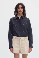 Camisa cropped de manga larga negra con estampado de lunares blancos, cuello camisero, cierre frontal de botones y bolsillos plaqué en el pecho.