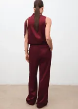 Pantalón wide leg de tiro medio en tejido satinado color bordó, con pinzas delanteras, trabillas, bolsillos laterales y cierre oculto con botón, gancho y cremallera.