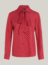 Blusa roja con estampado de rombos blancos, cuello con lazo y mangas largas con puños abotonados.