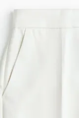 Pantalón de vestir blanco con cintura clásica, cierre con botón oculto y corchete. Presenta bolsillos al bies, bolsillo trasero decorativo y piernas amplias con pliegues marcados adelante y atrás.