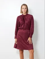 Vestido corto color borgoña con estampado geométrico, de gasa laminada con cuello alto entrelazado, manga larga raglán, cintura elastizada y espalda con abertura ojal y botones.