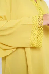 Blusón amarillo con escote en V y detalle de galón en cuello y mangas. Mangas anchas con volados y corte oversize.