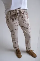 Pantalón de corte recto y ajuste holgado, confeccionado en tela beige con estampado floral en tonos marrones. Presenta cintura elástica con cordón ajustable y ruedos doblados.