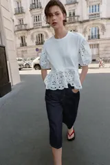Camiseta blanca de manga corta abullonada y cuello redondo, con detalles de bordados perforados y bajo con doble volante.