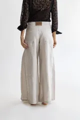 Pantalón de lino color greige, de piernas anchas, con cadera al cuerpo y cintura media. Presenta apliques de lino rayado en los costados.