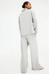 Buzo en tejido liviano color gris melange, con cuello camisero, tapeta con botones frontales, hombros caídos y puños acanalados.