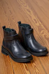 Bota corta de cuero color chocolate, con paneles frontales de gamuza en un tono más oscuro. Presenta una tira decorativa sobre el empeine, cierre lateral y suela de goma negra con plataforma baja.