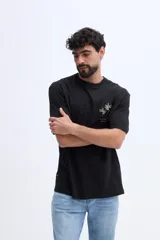 Remera oversize Brooksfield de color negro, confeccionada en 100% algodón, de manga corta y corte relajado. Cuenta con un diseño estampado en relieve en la espalda que representa flores abstractas y texto descriptivo en tono verde militar.
