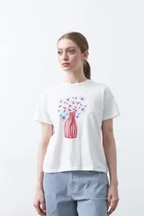 Remera blanca de manga corta con estampado frontal de un florero rojo con rayas verticales y un ramo de flores azules y rojas.