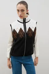 Chaleco con cierre frontal y cuello alto, que combina una parte superior acolchada con diseño de rombos en tonos blanco y marrón, y una parte inferior de corderito negro.