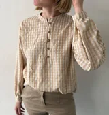 Blusa color beige con estampado a cuadros, cuello mao, mangas largas abullonadas y cierre frontal con botones.