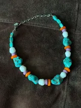 Collar corto compuesto por cuentas grandes de piedra turquesa irregular, alternadas con cuentas circulares blancas, naranjas y lilas.