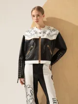 Chaqueta corta de cuero negra y blanca con bordados plateados en el canesú y cordones trenzados en las mangas.