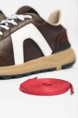 Zapatillas deportivas marrones con detalles en blanco y suela color caramelo.