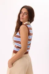 Top tejido sin mangas con diseño a rayas horizontales en tonos azul marino, celeste y crema. Presenta cuello tipo polo con tapeta de botones frontal y terminaciones acanaladas en el ruedo y sisas.