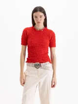 Top rojo de manga corta con textura fruncida en toda la prenda, cuello semi alto y terminaciones con volados en el cuello y los puños.
