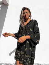 Túnica corta negra con estampado dorado de hojas y motivos geométricos, escote en V y mangas acampanadas.