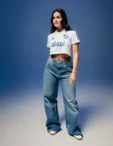 Camiseta de fútbol Umbro del Club Nacional de Football, modelo Home 2026 para mujer. Diseño blanco tipo crop con cuello polo, detalles en azul y rojo en cuello y mangas, logo de Umbro, escudo del club y sponsor Antel en el frente.