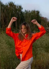 Camisa de manga larga color naranja vibrante, con cuello camisero y botones frontales blancos. Corte holgado.