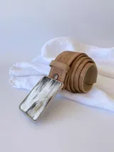 Cinto de cuero color camel con forro de cuero y hebilla rectangular de guampa con borde metálico trenzado. Cuenta con broche suizo intercambiable.