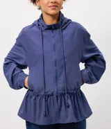 Campera cortaviento de poliéster color azul, con diseño peplum en la cintura, capucha ajustable con cordones y cierre frontal. Presenta mangas largas y un corte funcional y liviano.