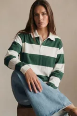 Sweater estilo polo de corte oversize, con diseño de rayas horizontales anchas en tonos camel y bordó. Presenta cuello camisero con cierre frontal parcial y mangas largas con puños ajustados.