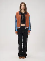Campera estilo bomber Mutma Satifo, de diseño colorblock con cuerpo en color óxido y mangas celestes con detalles en azul marino. Cuenta con cuello camisero, cierre frontal, puños y ruedo elásticos rayados, y un parche gráfico en el pecho.