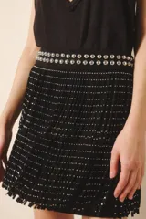 Falda corta negra de cuero con diseño de flecos y remaches metálicos plateados. La cintura es ancha y está adornada con tachas bombé.