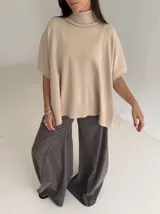 Poncho de tejido de punto color marrón chocolate, con cuello alto tipo polera y mangas cortas amplias. Presenta un diseño holgado con terminaciones acanaladas en el ruedo.